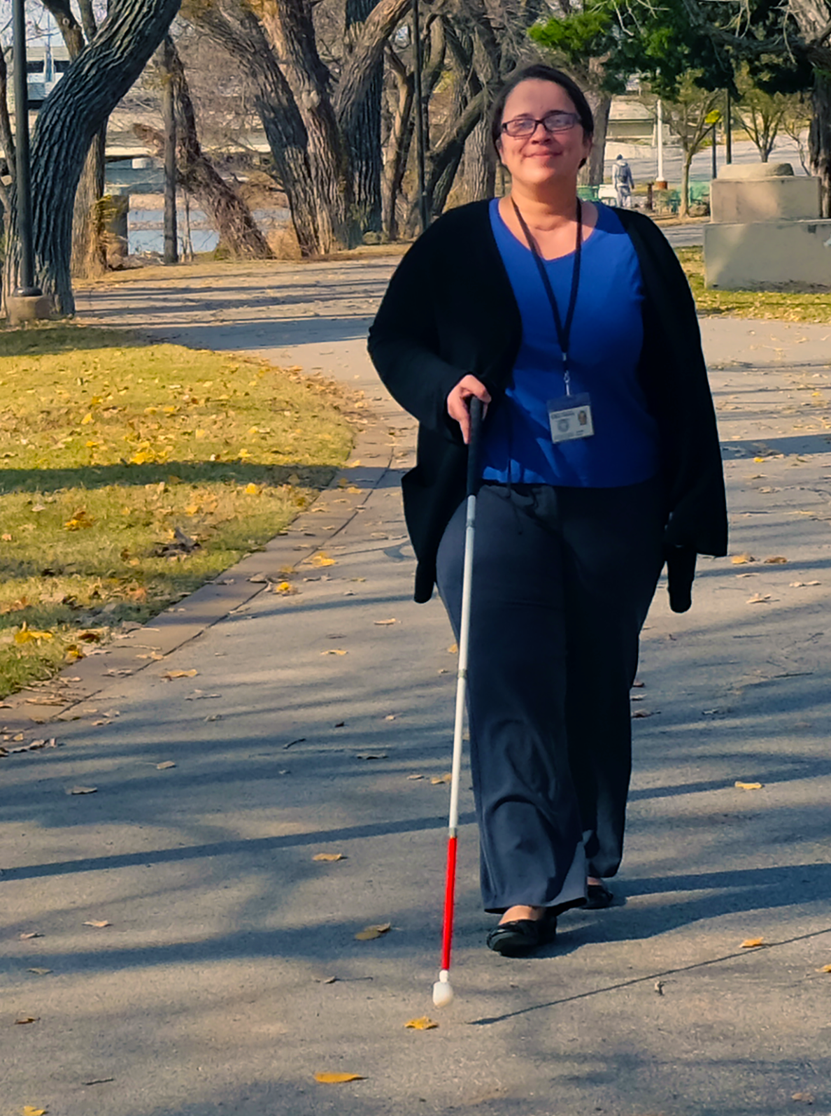 A woman who uses a white cane is walking outside.